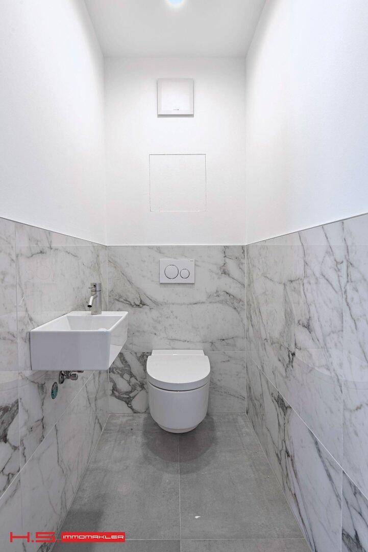 Modernes Gäste-WC mit Marmoroptik-Fliesen, wandhängendem WC und kleinem Waschbecken.