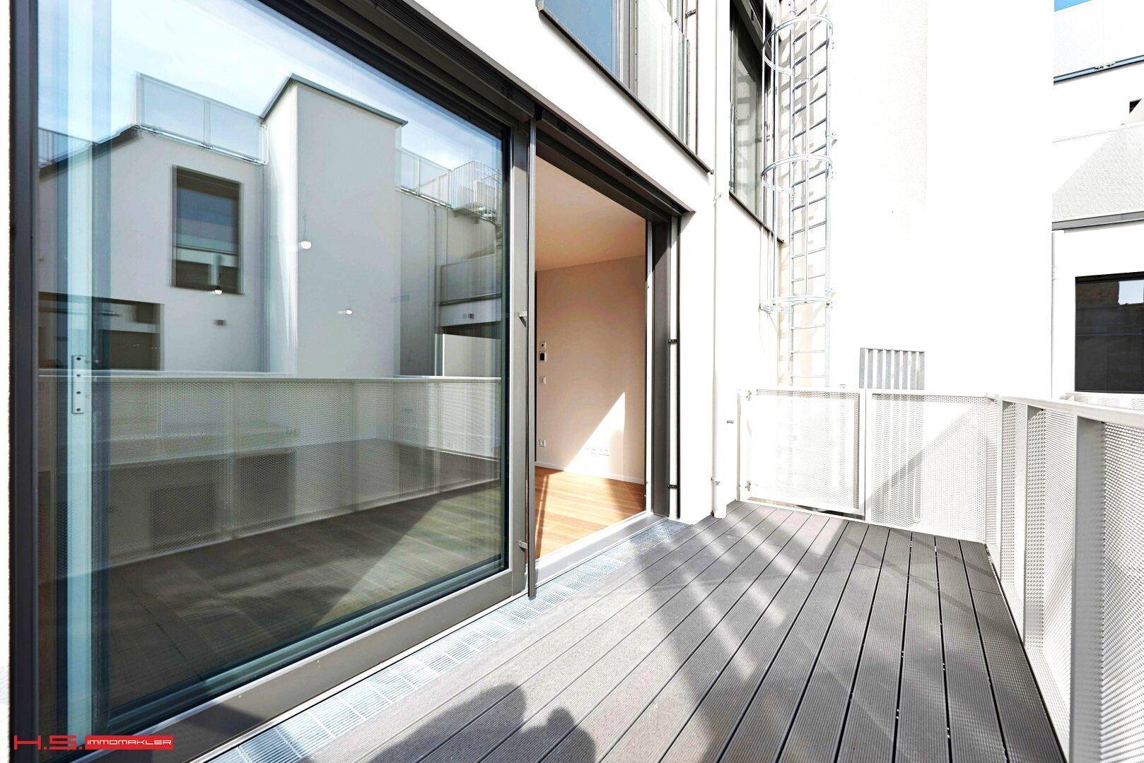 Moderner Balkon mit dunklem Bodenbelag und Zugang zum Innenraum durch eine große Glasschiebetür.
