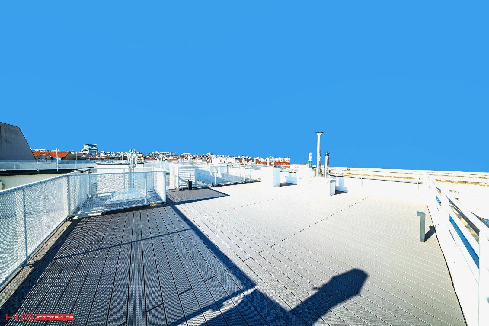 Weitläufige Dachterrasse mit moderner Holzoptik-Bodenbelag und weitem Blick über die Stadt.
