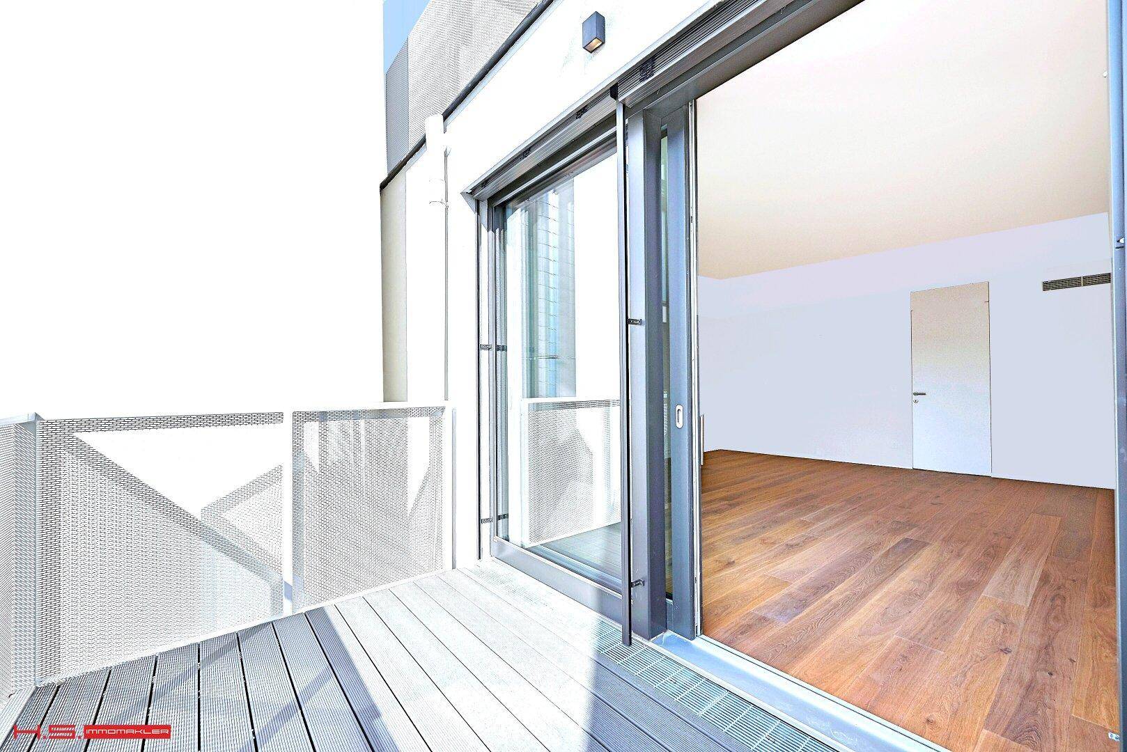 Moderner Balkon mit Holzboden und Blick auf die Umgebung, zugänglich vom Innenraum.