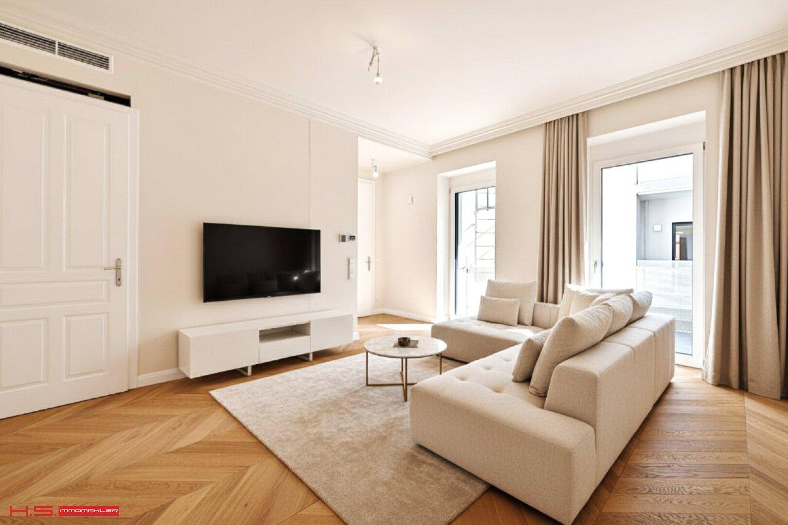 Gemütliches Wohnzimmer mit hellem Parkettboden, bequemen Sofas und Zugang zu einem Balkon.