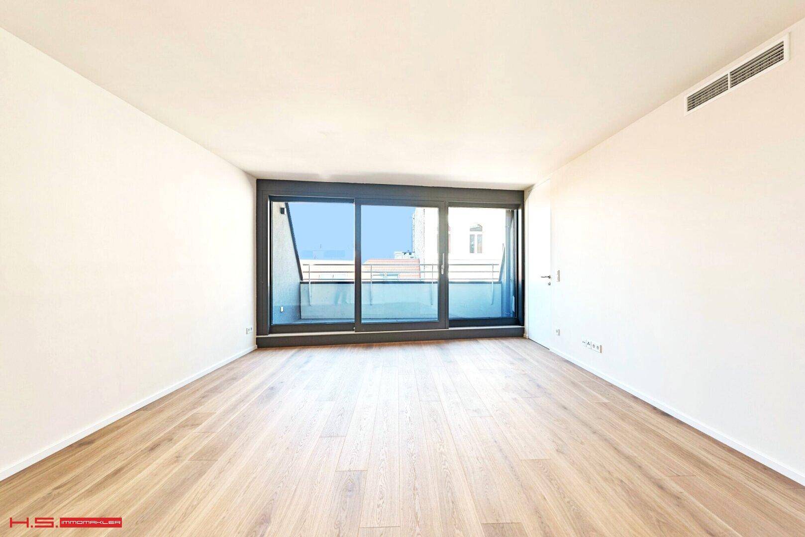 Geräumiger, heller Raum mit Holzboden und großzügigem Zugang zu einem Balkon.