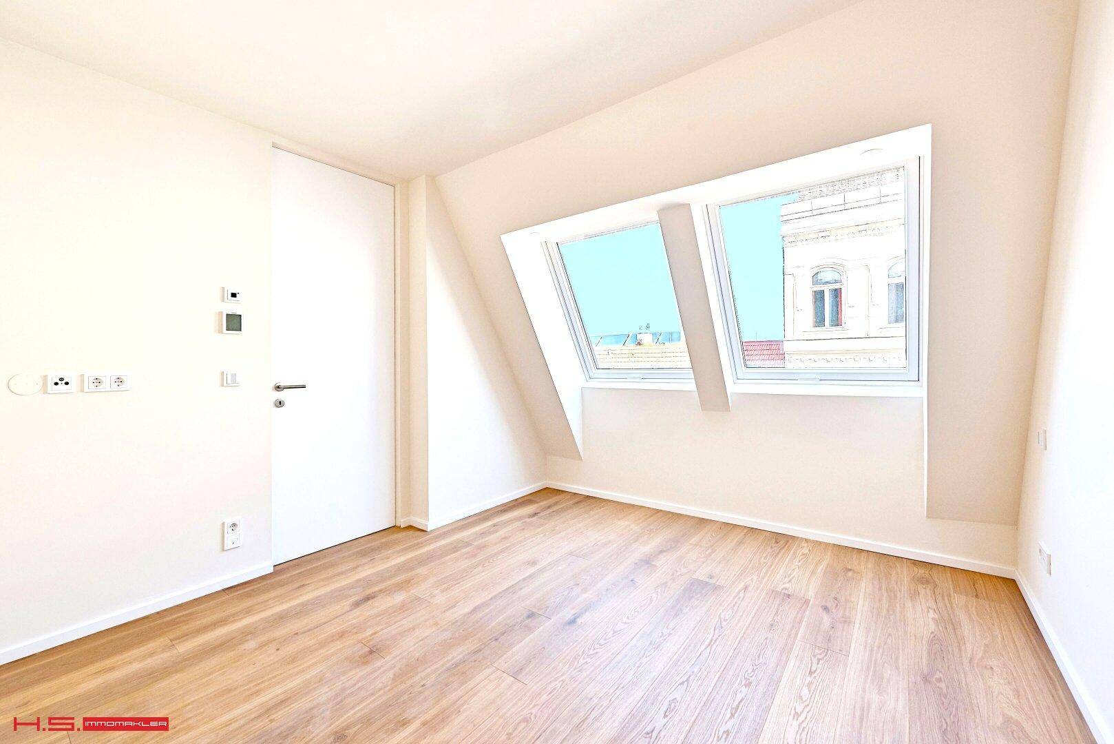 Heller Raum im Dachgeschoss mit Holzboden, Dachschrägen und großen Dachfenstern.