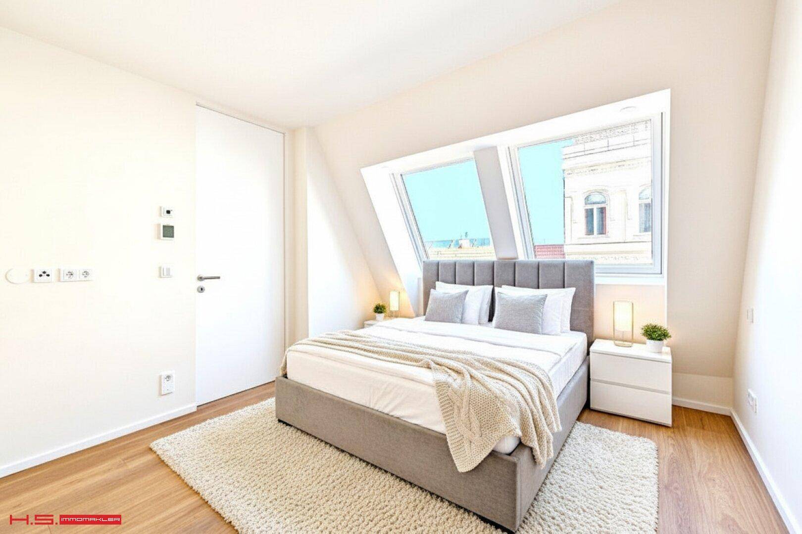 Helles Schlafzimmer im Dachgeschoss mit Holzboden, Dachschrägen und großen Dachfenstern.