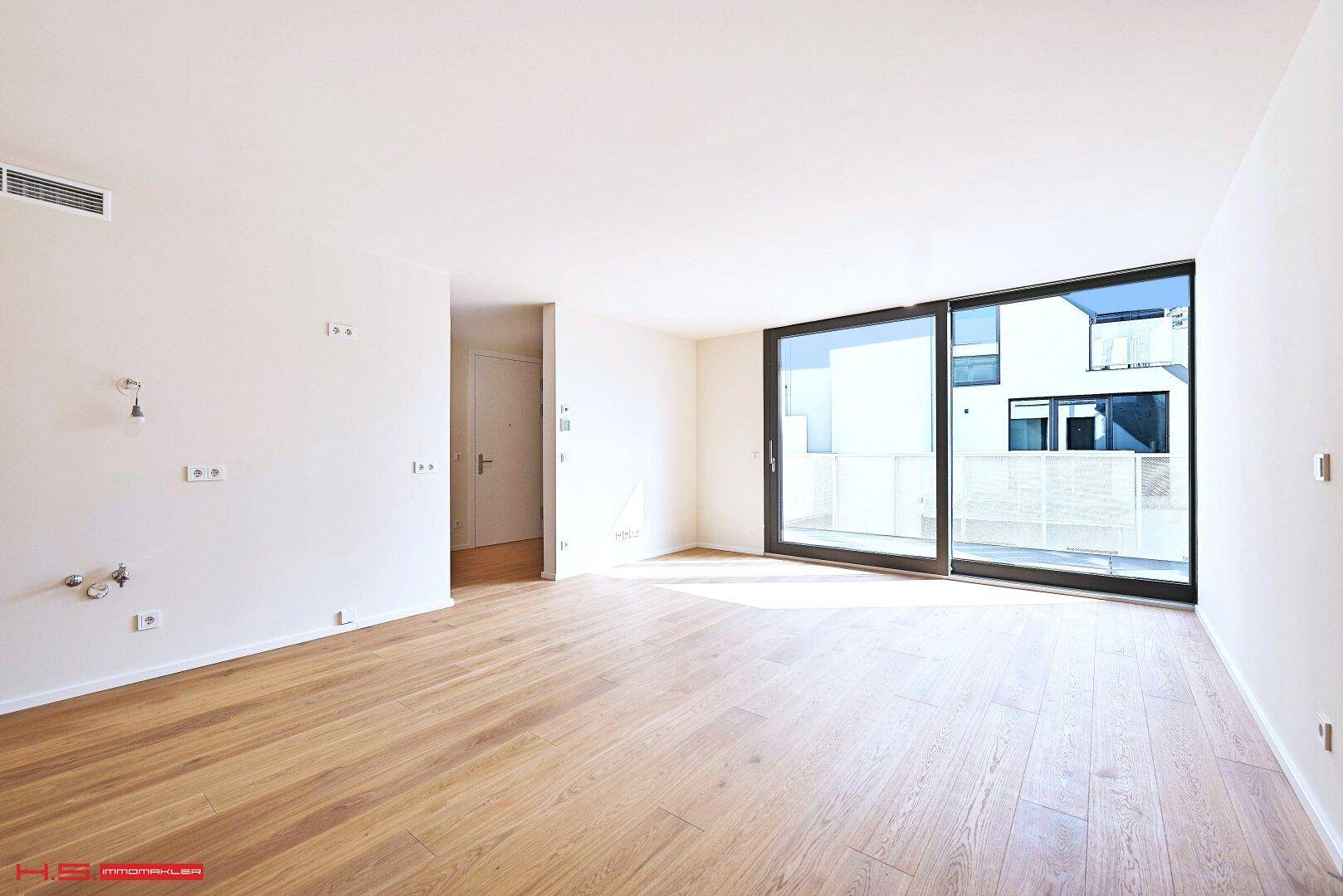 Leerer, heller Wohnbereich mit Holzboden und großen Schiebetüren, die viel Tageslicht hereinlassen.