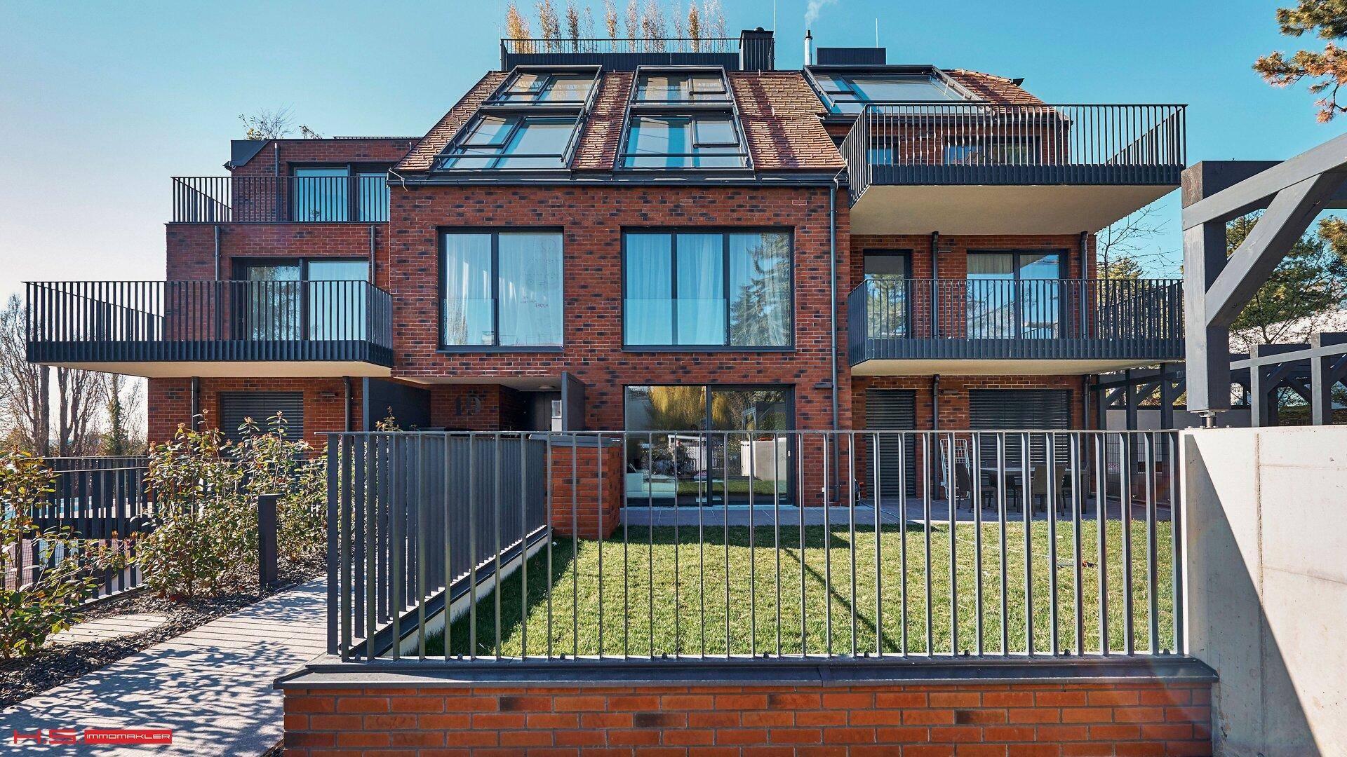 Moderne Wohnanlage mit Ziegelfassade, großen Fenstern und mehreren Balkonen sowie Dachterrassen.