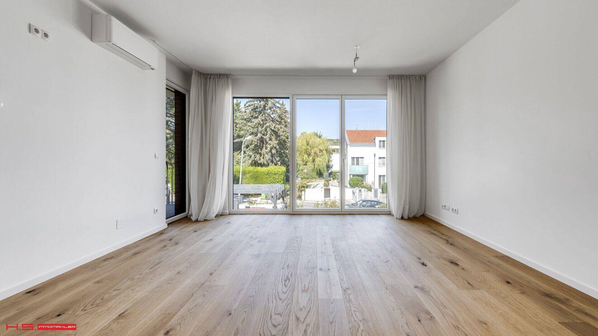 Lichtdurchfluteter Raum mit breiten Fenstern und Eichenparkett, ideal für einen Wohnbereich.