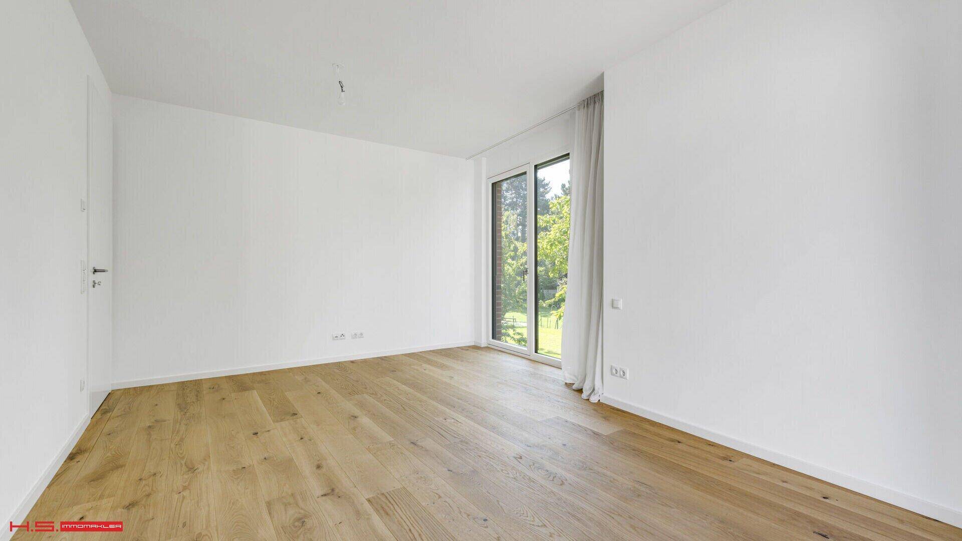 Unmöblierter Raum mit hellem Eichenparkett und großem Fenster, das viel Tageslicht hereinlässt.