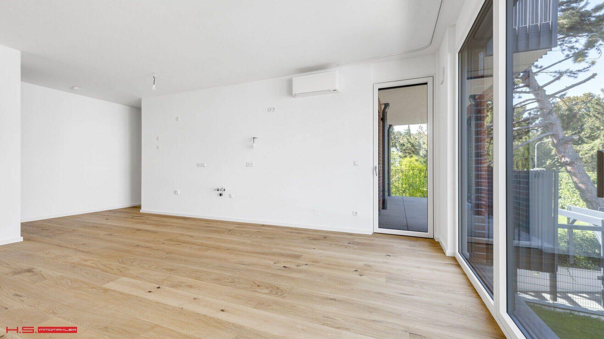 Heller, unmöblierter Raum mit Eichenparkett und Zugang zu einem Balkon, ausgestattet mit Klimaanlage.