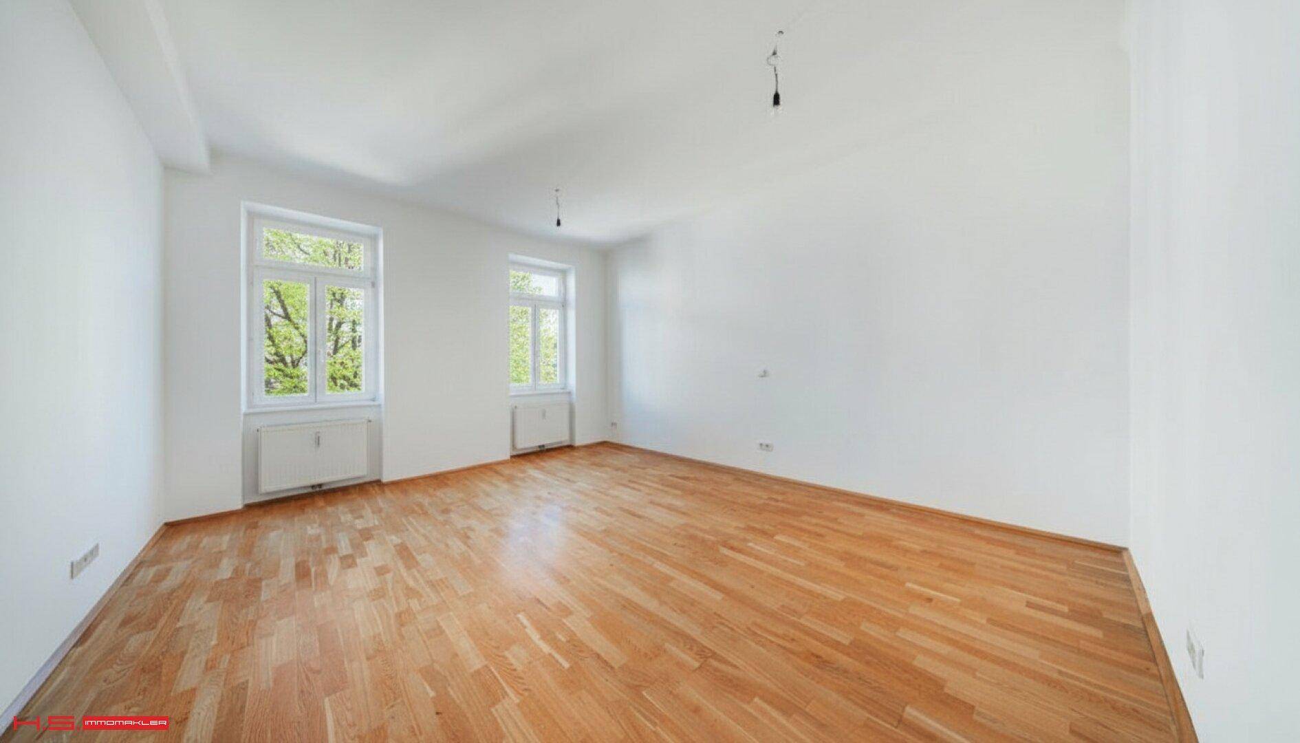 Geräumiges, helles Zimmer mit Parkettboden und zwei großen Fenstern, bereit zur individuellen Gestaltung.