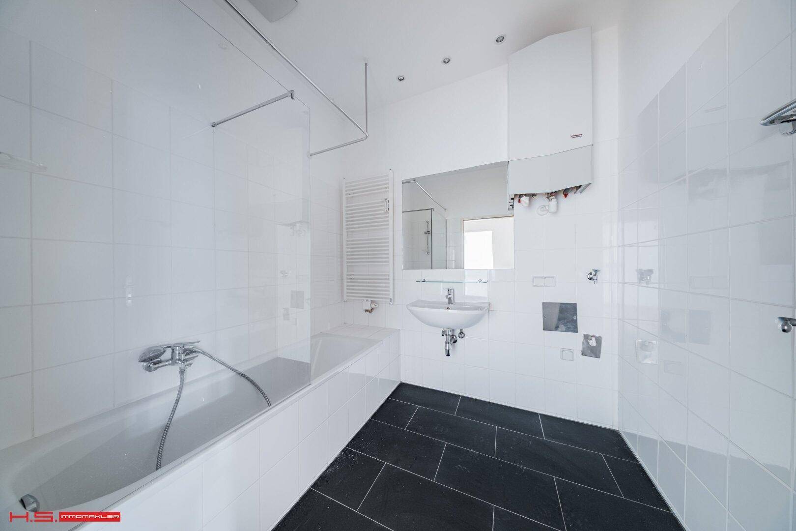 Modernes Badezimmer mit Badewanne, Dusche, Waschbecken und dunklen Bodenfliesen, hell gefliest.