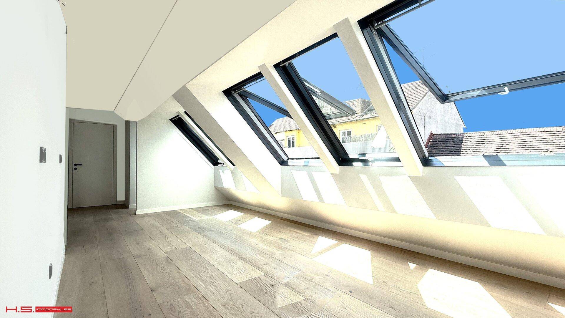 Heller Dachraum mit mehreren Dachfenstern und Holzboden, der viel natürliches Licht hereinlässt.