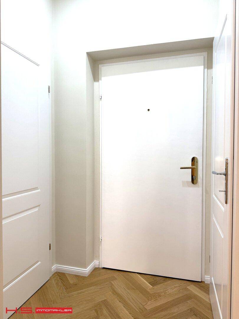 Eingangstür der Wohnung mit Fischgrätparkett im Flurbereich und hellen Wänden.
