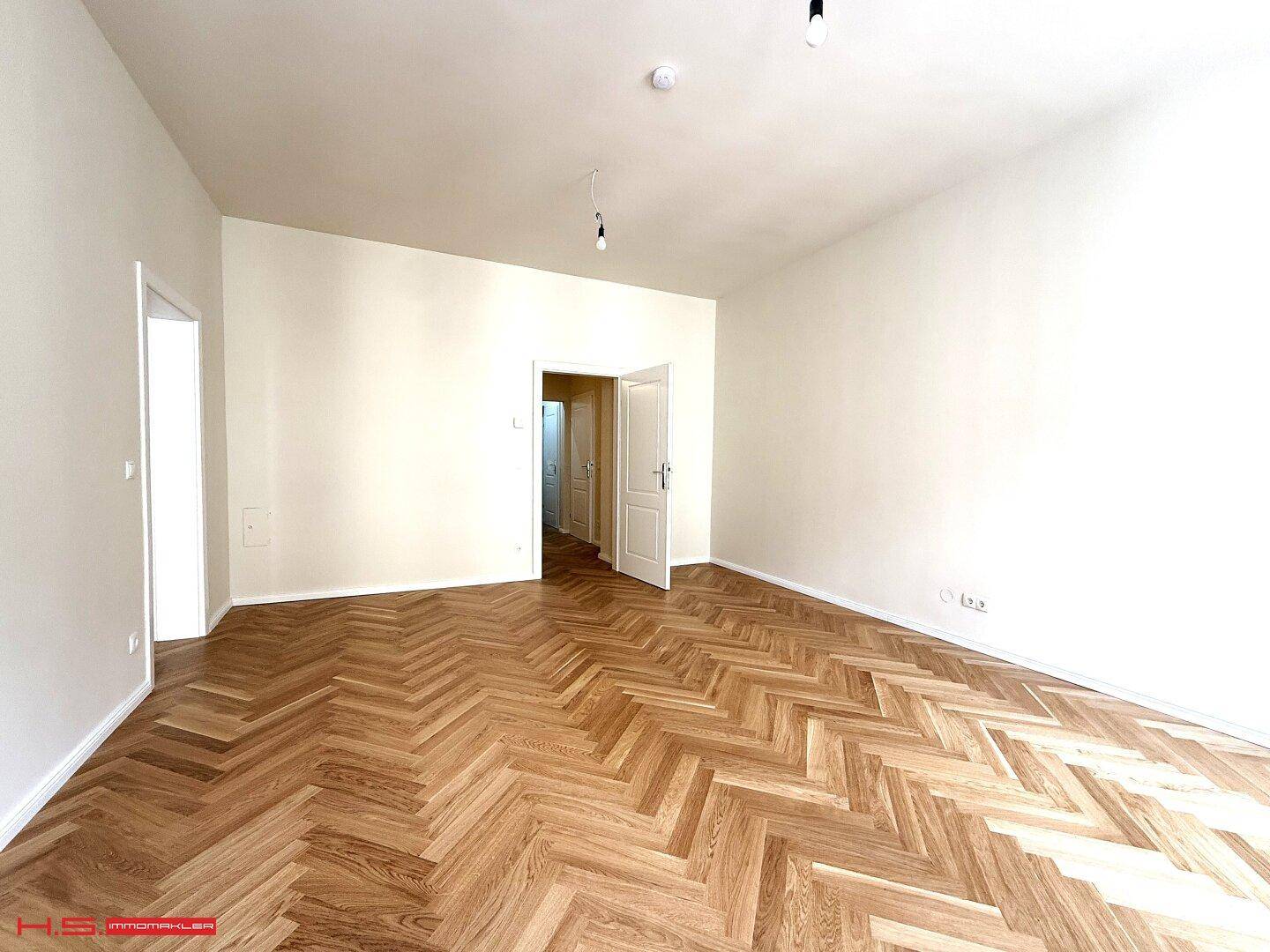 Geräumiges Wohnzimmer mit Fischgrätparkett und Zugang zu weiteren Zimmern der Wohnung.