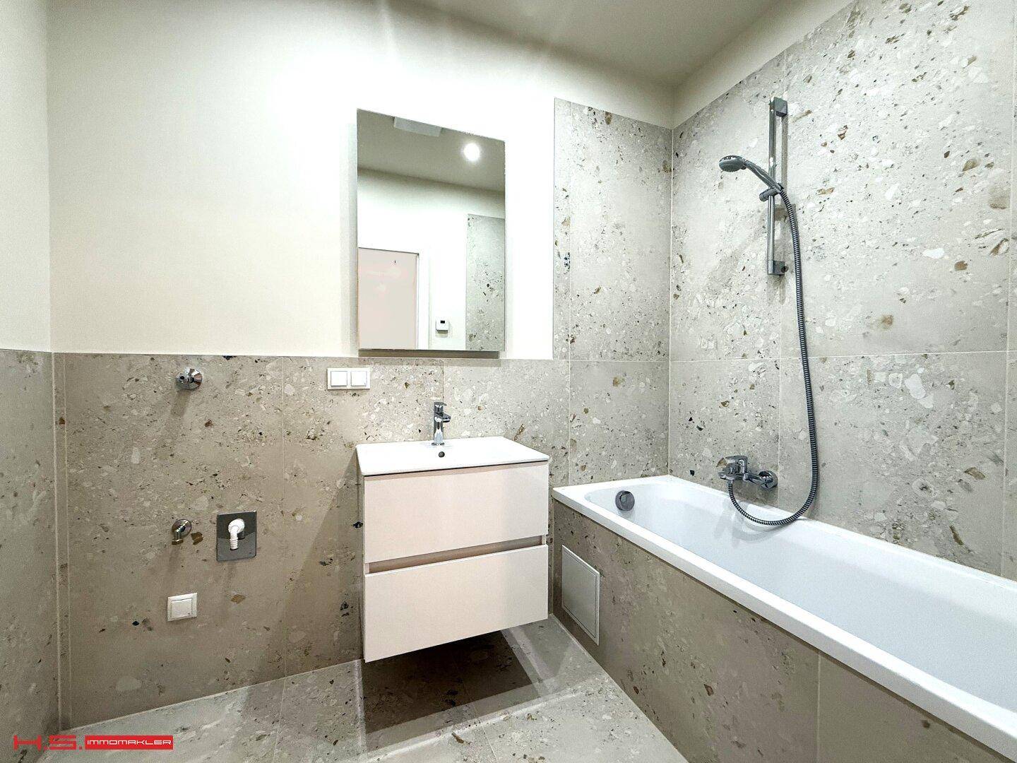 Modernes Badezimmer mit Badewanne, Waschtisch und hellen, großformatigen Fliesen an den Wänden.