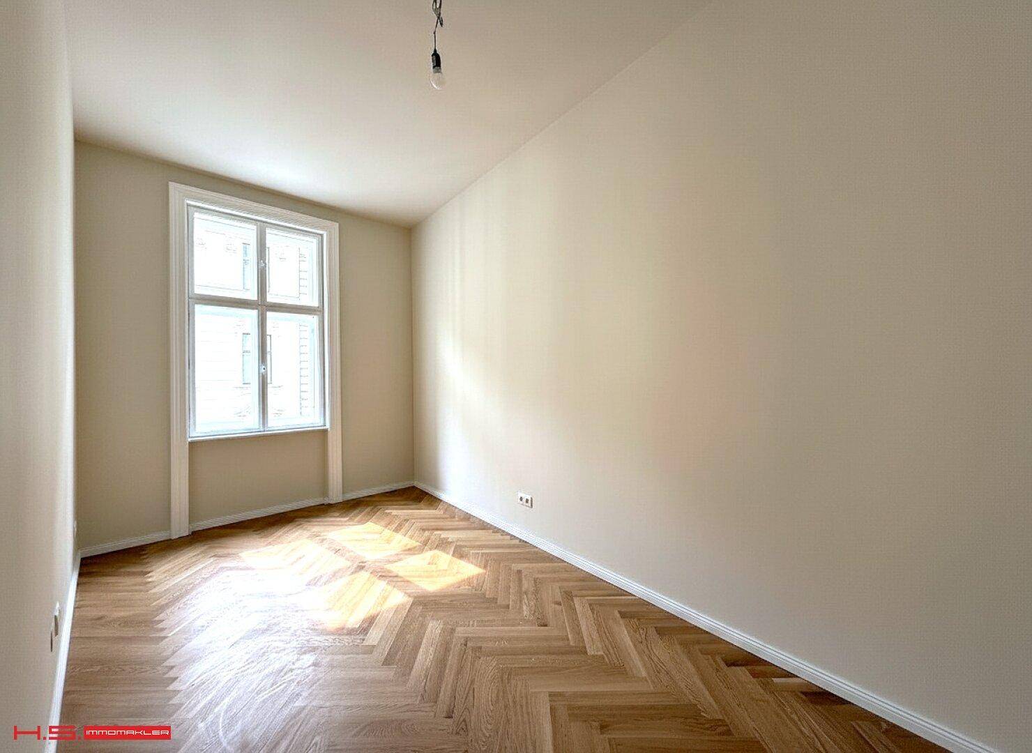 Sonniger Raum mit Fischgrätparkett und einem großen Fenster für viel Tageslicht.