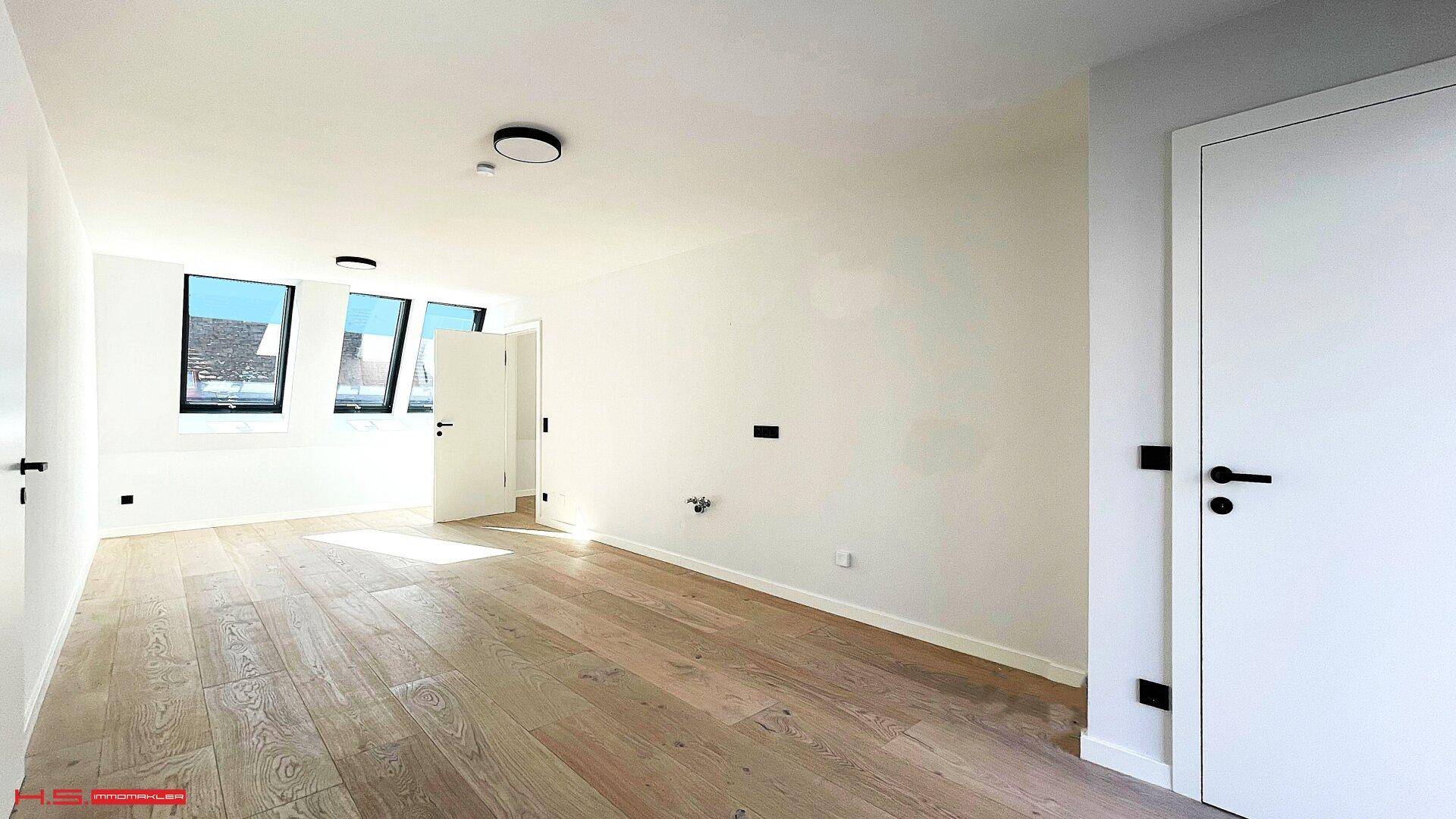 Geräumiger, heller Raum im Dachgeschoss mit Holzboden und mehreren schrägen Fenstern.