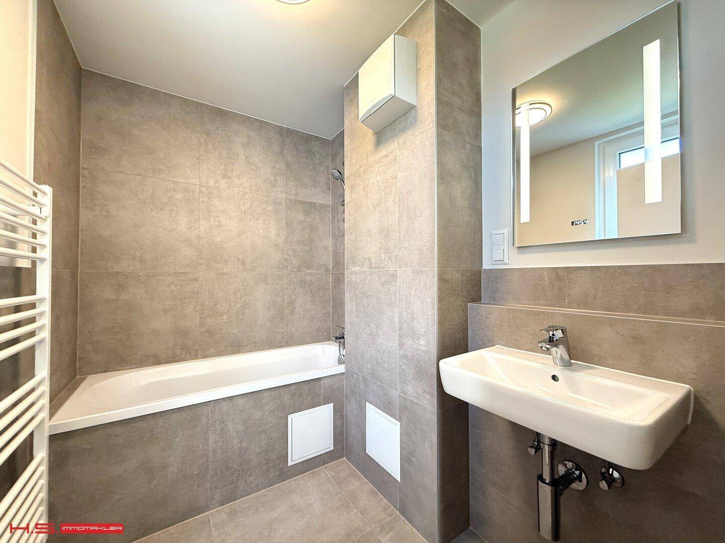 Modernes Badezimmer mit Badewanne, Fliesenboden und beheiztem Handtuchhalter.