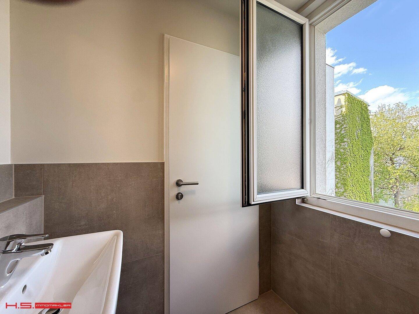 Helles Badezimmer mit Waschbecken und Fenster, das viel Tageslicht hereinlässt.
