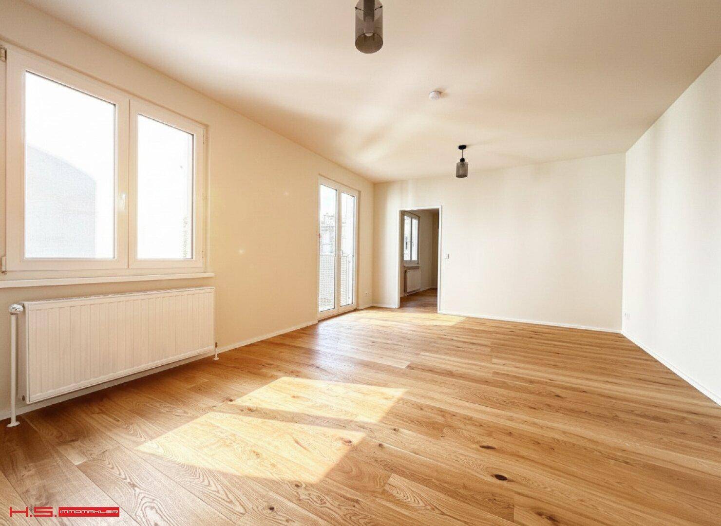 Großes, helles Wohnzimmer mit Holzboden und Zugang zu einem Balkon, bereit zur Einrichtung.