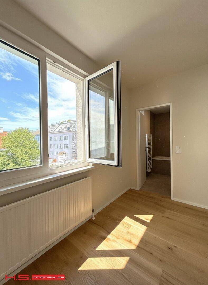 Helles Zimmer mit Holzboden und großem Fenster, mit Blick auf die Stadt und Zugang zum Bad.