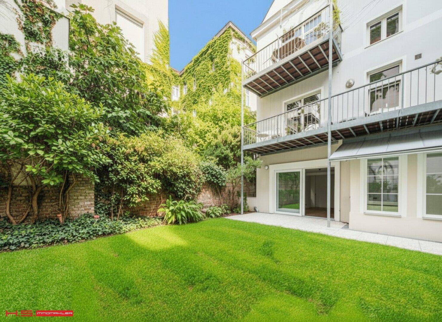 Ruhiger Gartenbereich mit gepflegtem Rasen und Zugang zu einer hellen Terrasse und Balkonen.