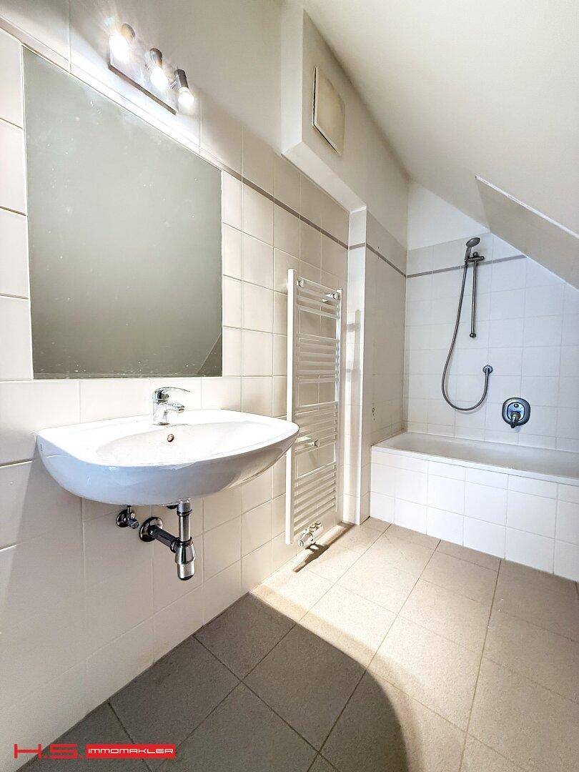 Modernes Badezimmer mit weißen Fliesen, Badewanne, Dusche und beheiztem Handtuchhalter unter einer Dachschräge.