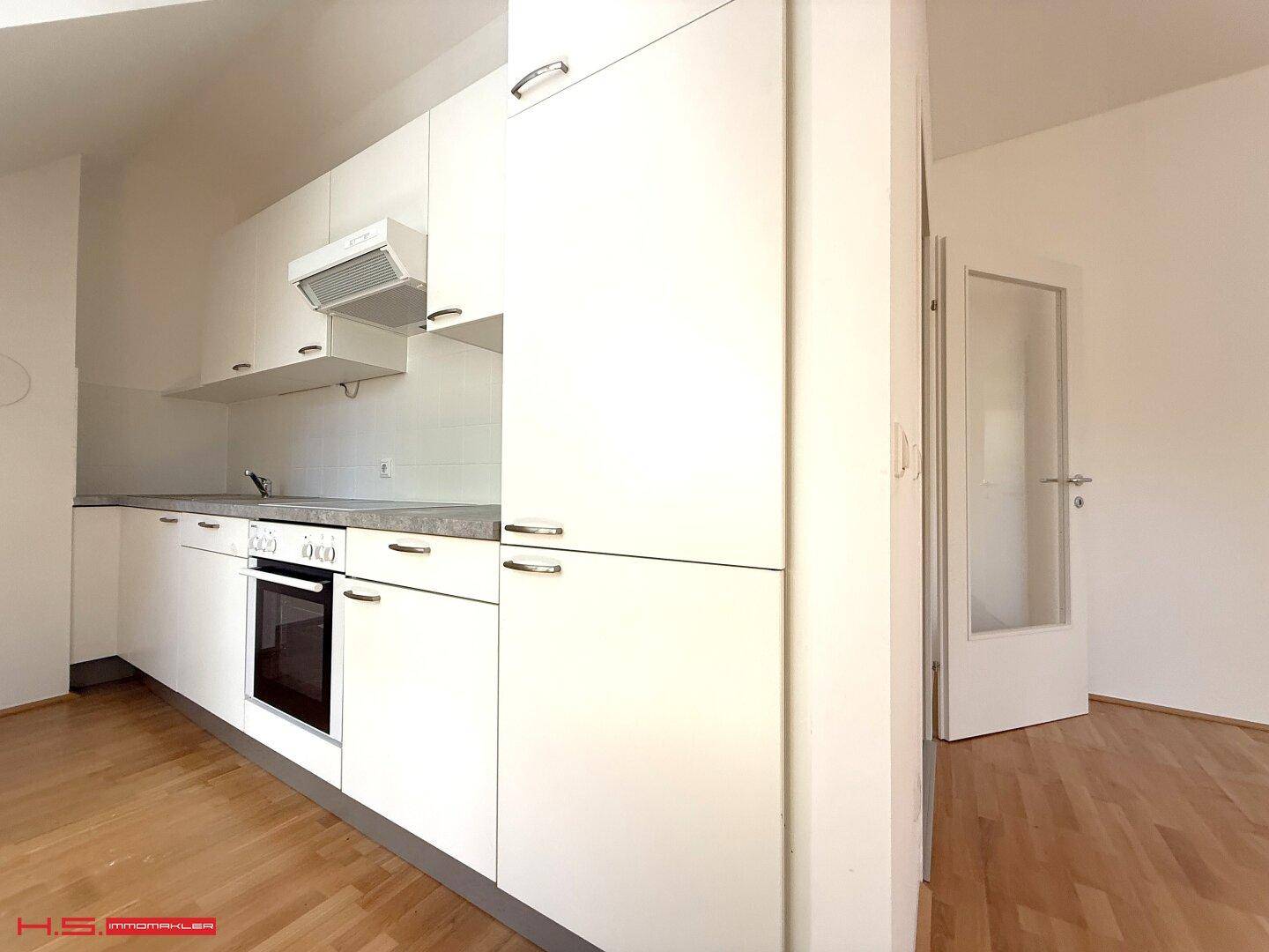 Kompakte Einbauküche mit weißen Schränken, integriertem Backofen und Dunstabzugshaube, ideal für kleine Wohnungen.