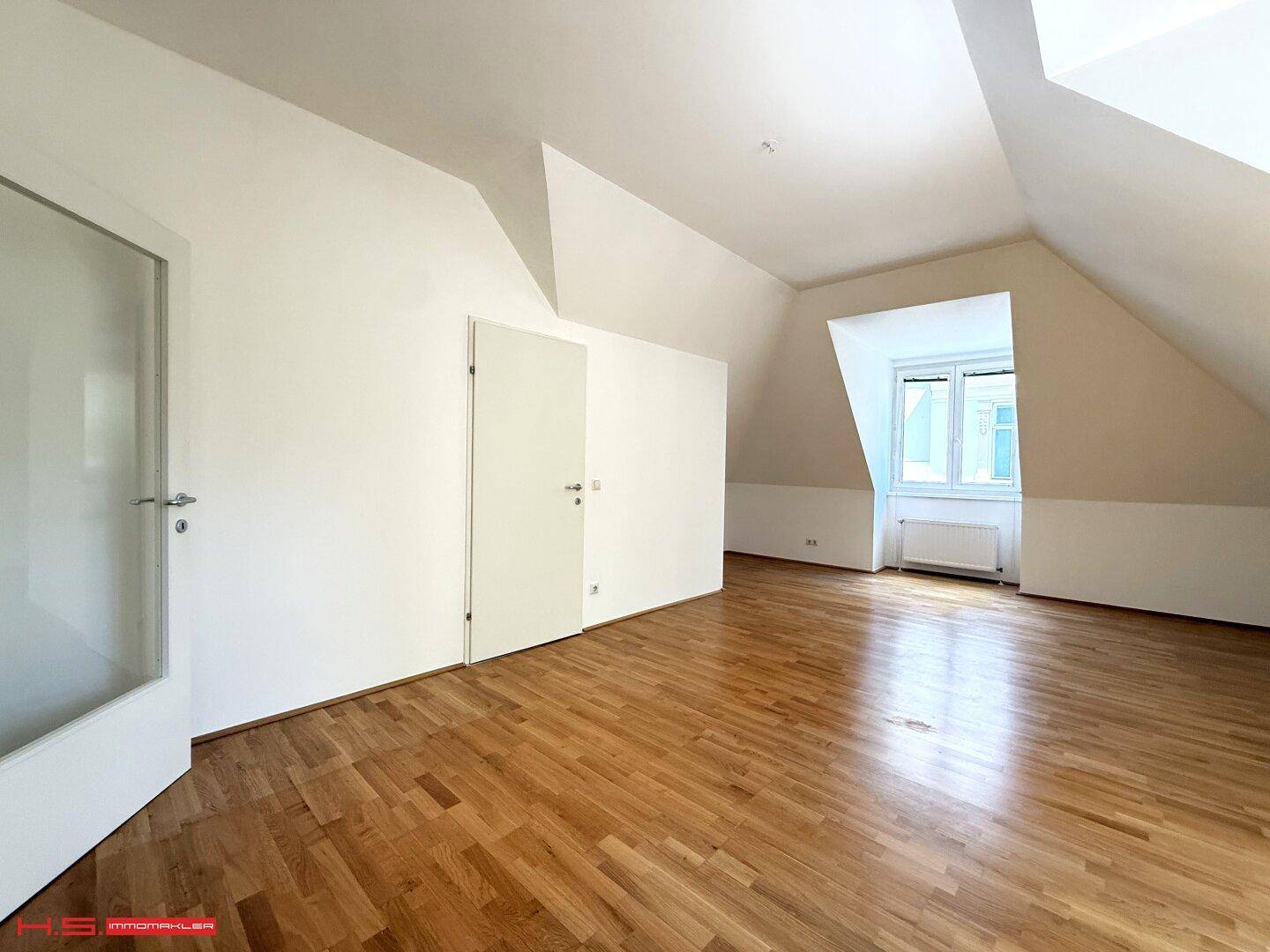 Heller Dachgeschossraum mit Holzboden, schrägen Wänden und einer Tür mit Glaseinsatz, bietet vielseitige Nutzungsmöglichkeiten.