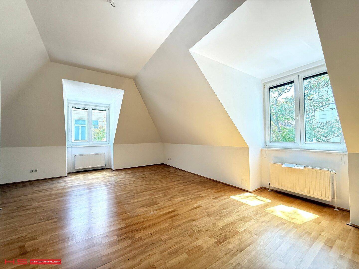 Helles Dachgeschosszimmer mit Holzboden und schrägen Wänden, durchflutet von natürlichem Sonnenlicht.