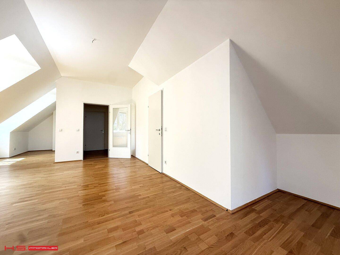 Geräumiger Innenraum im Dachgeschoss mit Holzboden, schrägen Wänden und Zugang zu weiteren Zimmern.