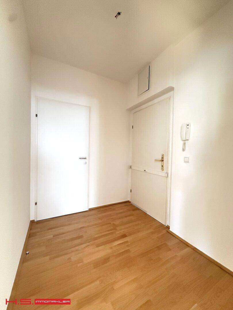 Heller Flur mit Holzboden und zwei Türen, ausgestattet mit einer Gegensprechanlage.