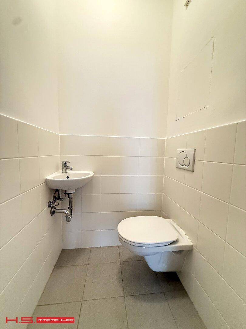 Kleines, hell gefliestes WC mit wandhängender Toilette und Handwaschbecken.