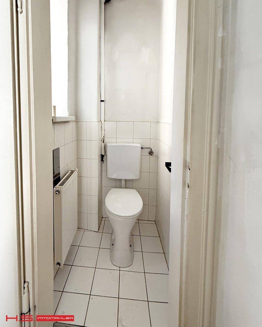 Separates WC mit Fenster, Toilette und Heizkörper, ausgestattet mit weißen Fliesen.