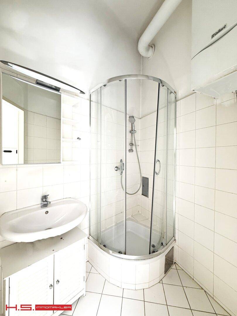 Helles Badezimmer mit Eckdusche, Waschbecken und Spiegelschrank, komplett gefliest.
