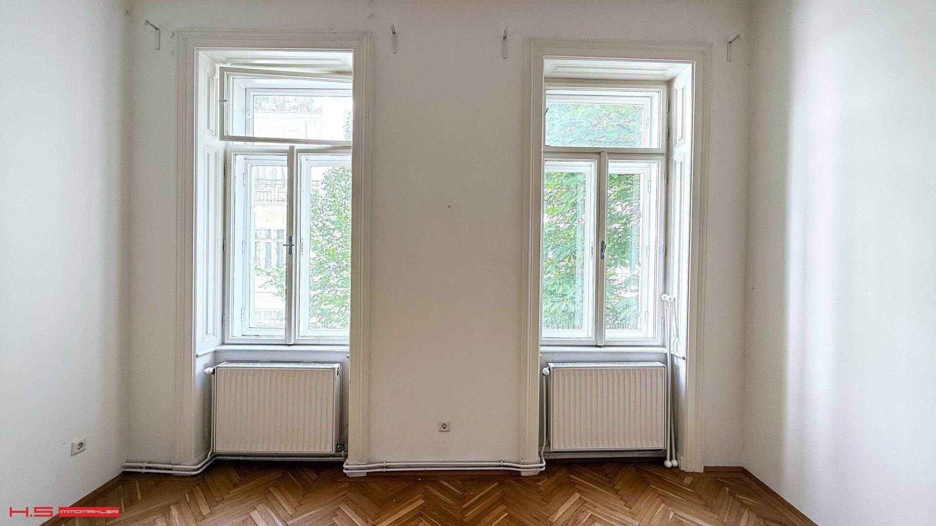 Helles Zimmer mit zwei hohen Fenstern und Fischgrätparkett, bietet viel Tageslicht.