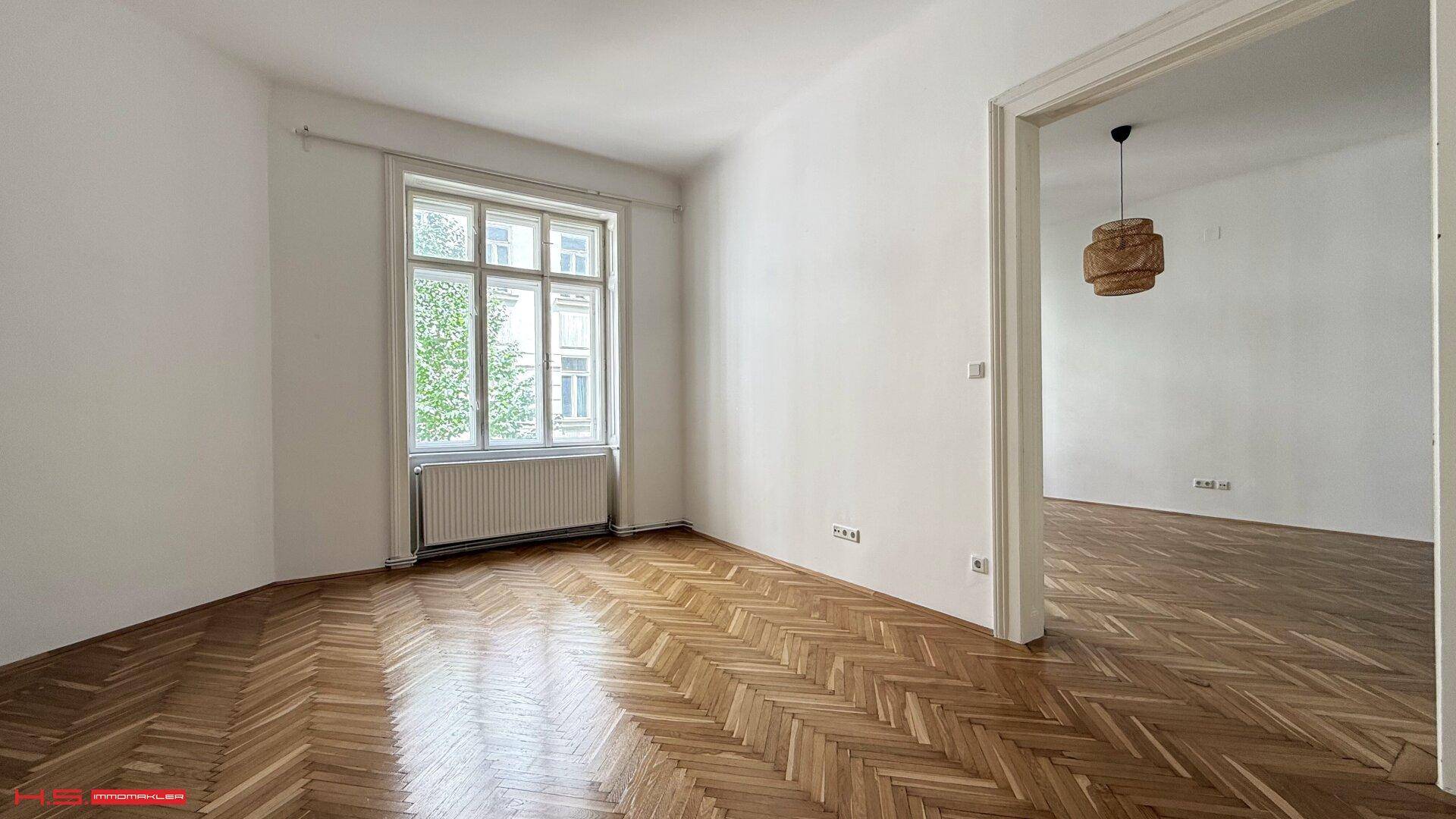 Helles Zimmer mit Fischgrätparkett und großem Fenster, bietet viel Tageslicht.