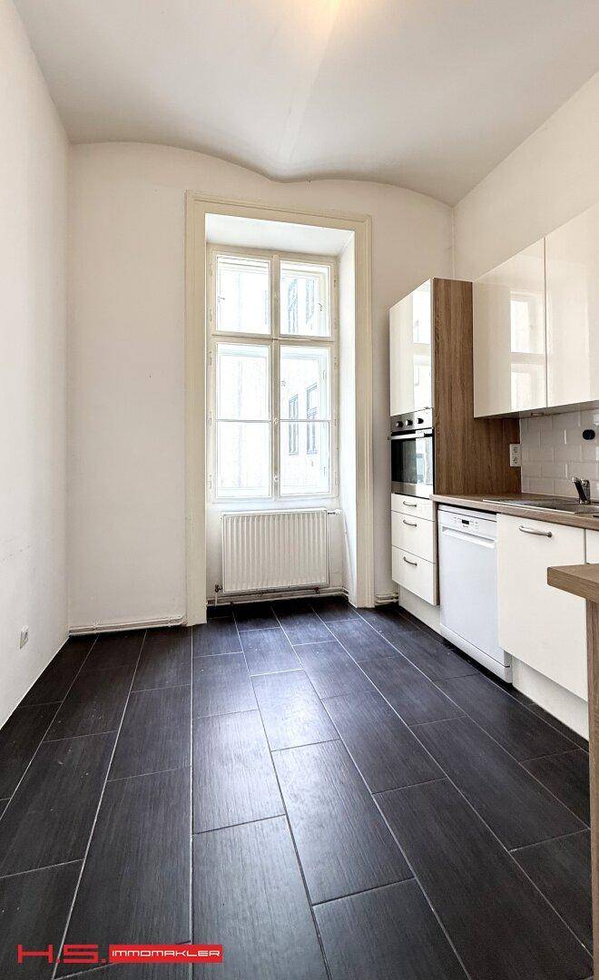 Helle Küche mit modernen weißen Schränken, dunklem Fliesenboden und großem Fenster.
