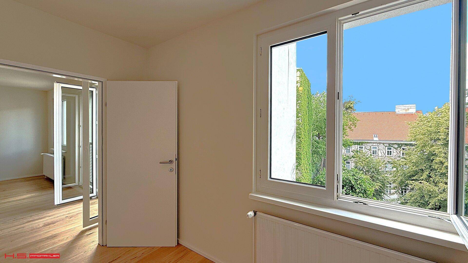 Lichtdurchfluteter Raum mit Holzboden und Blick ins Grüne durch das Fenster.