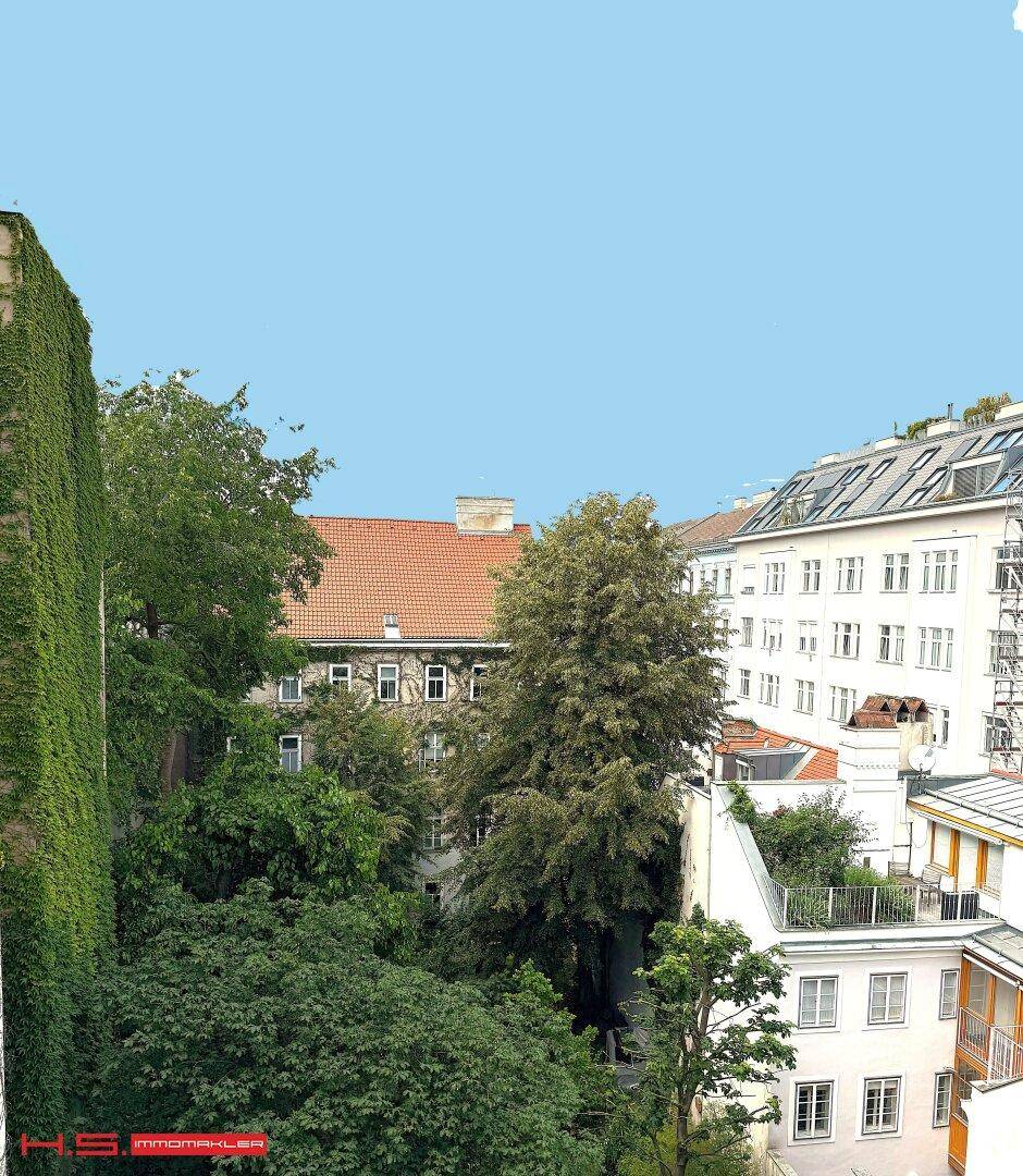 Blick aus dem Fenster auf grüne Bäume und die Dächer umliegender Gebäude.
