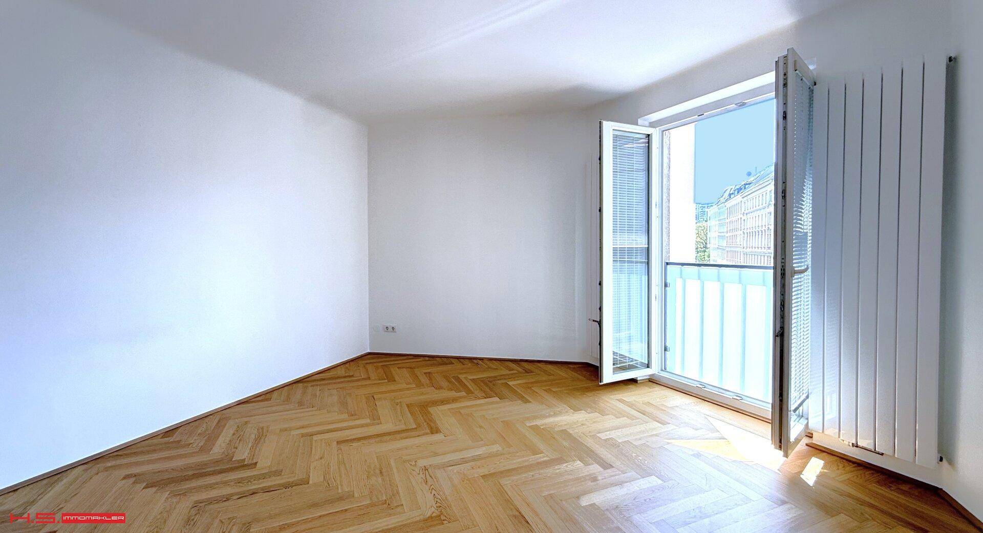 Geräumiges Zimmer mit Fischgrätparkett und Zugang zu einem französischen Balkon, der viel Licht hereinlässt.