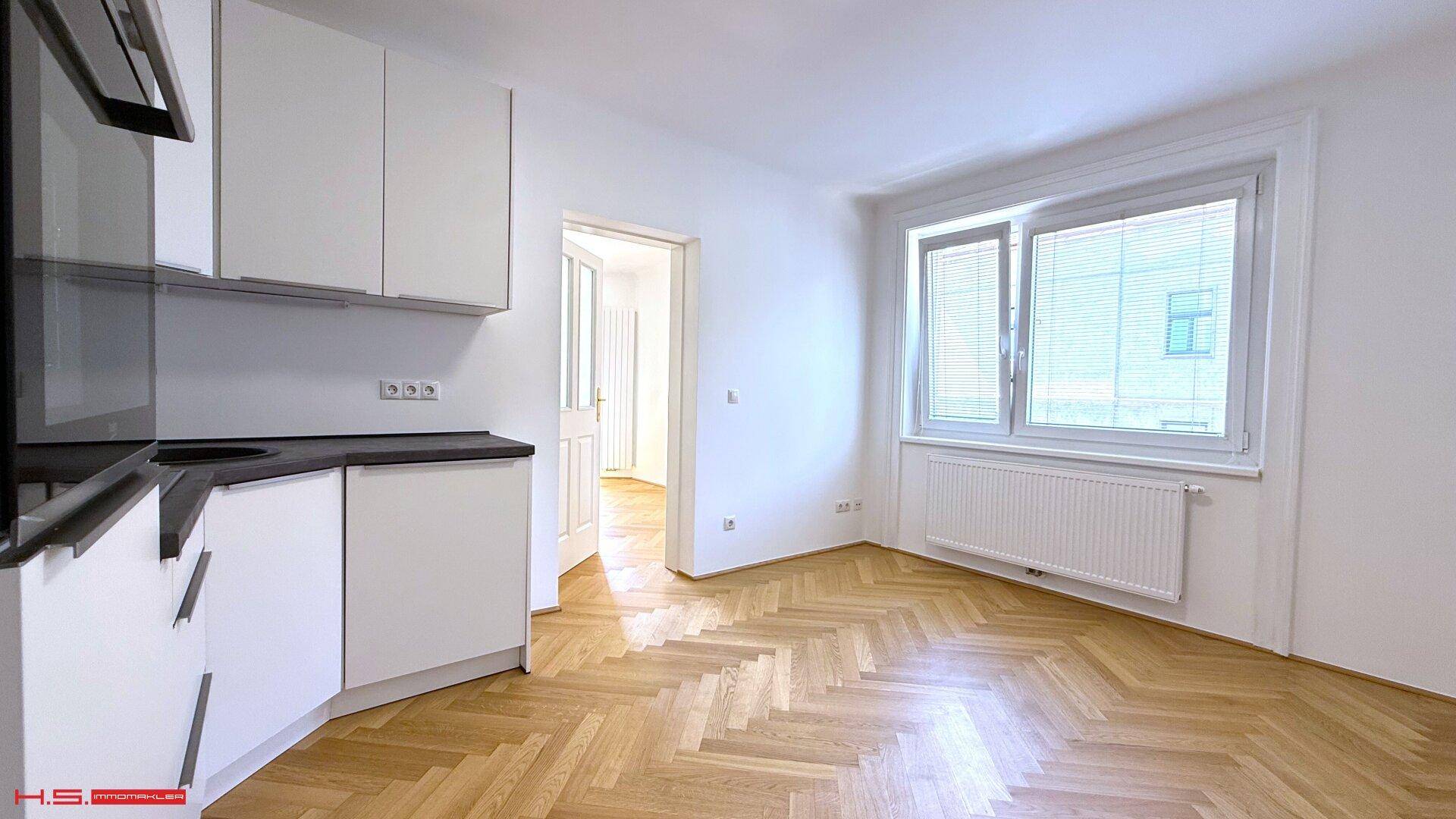 Offener Küchenbereich mit weißen Schränken, schwarzer Arbeitsplatte und Blick aus dem Fenster.