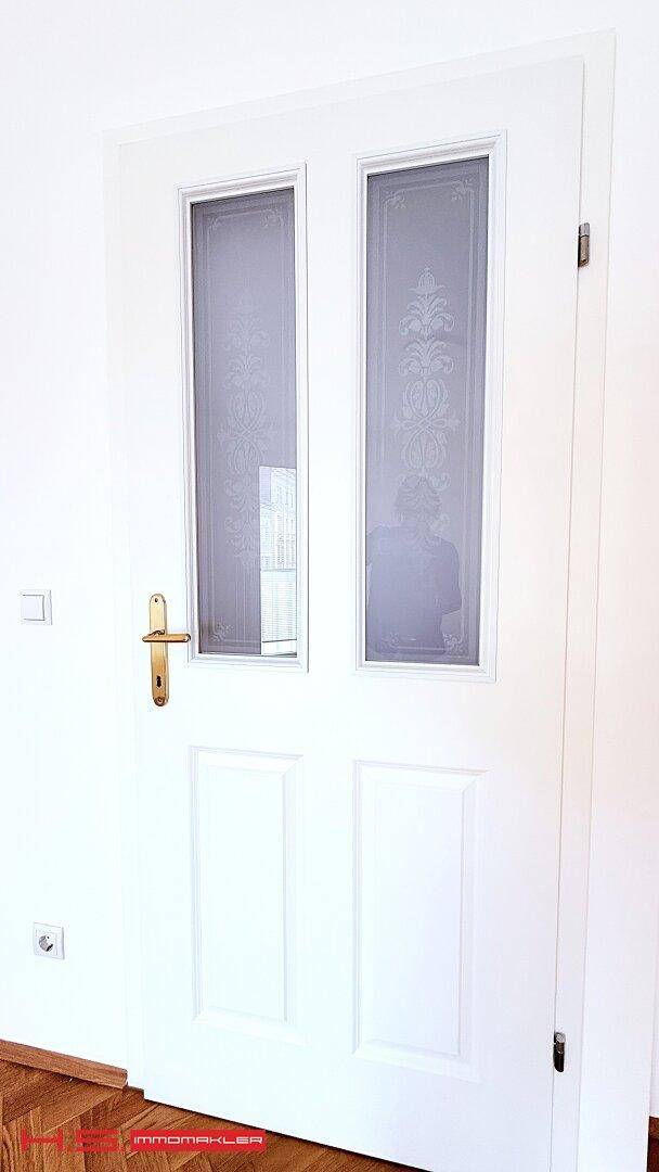 Nahaufnahme einer weißen Innentür mit Glaseinsätzen und einem eleganten goldenen Türgriff.