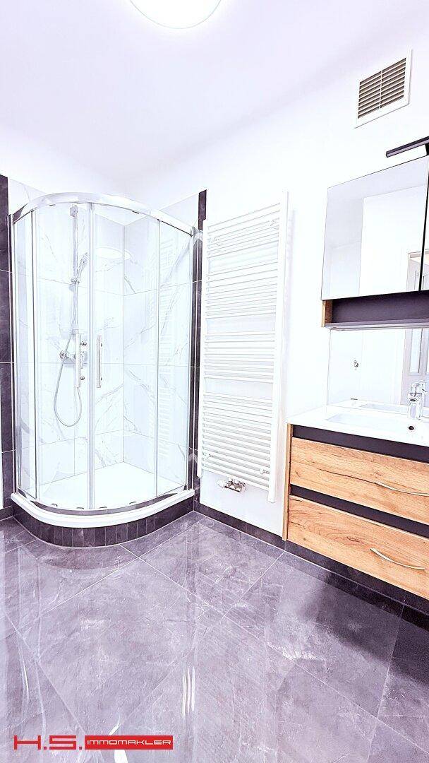 Modernes Badezimmer mit Eckduschkabine, Holzwaschtisch und beheiztem Handtuchhalter.