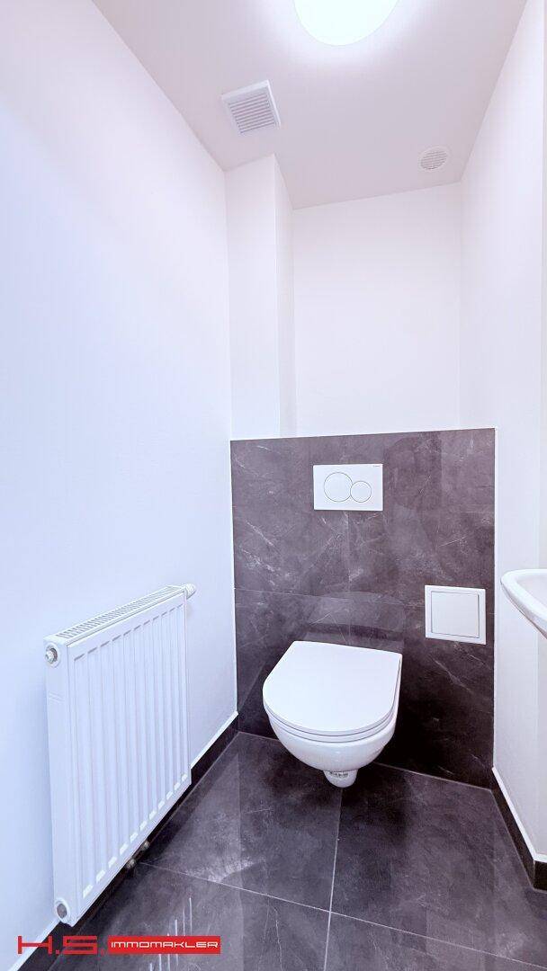 Separates WC mit wandhängender Toilette, kleinem Waschbecken und Heizkörper.