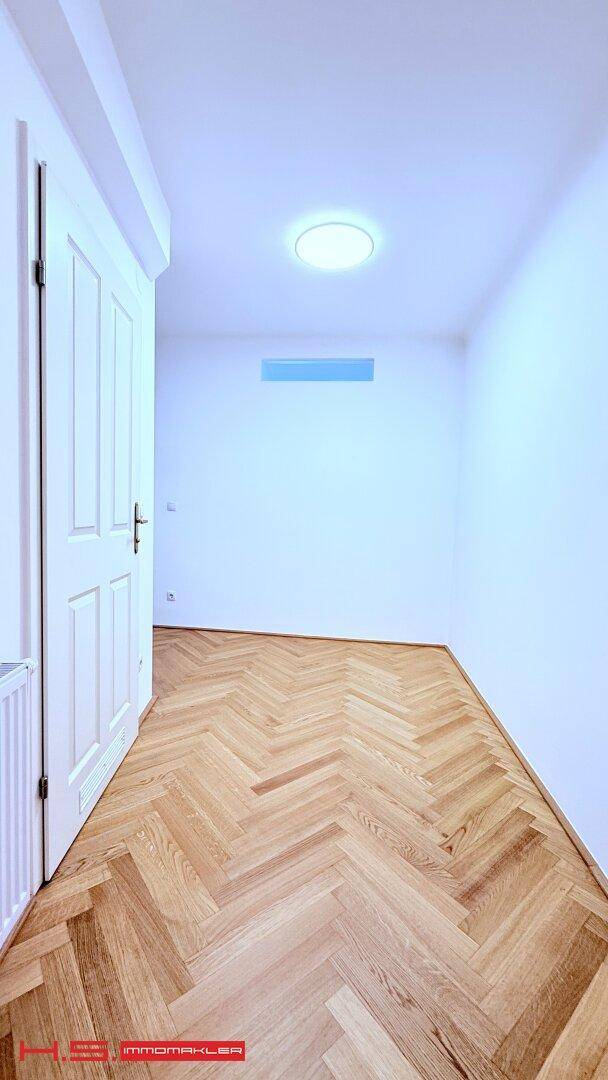 Heller Flur mit Fischgrätparkettboden und einer weißen Tür, beleuchtet von einer Deckenleuchte.