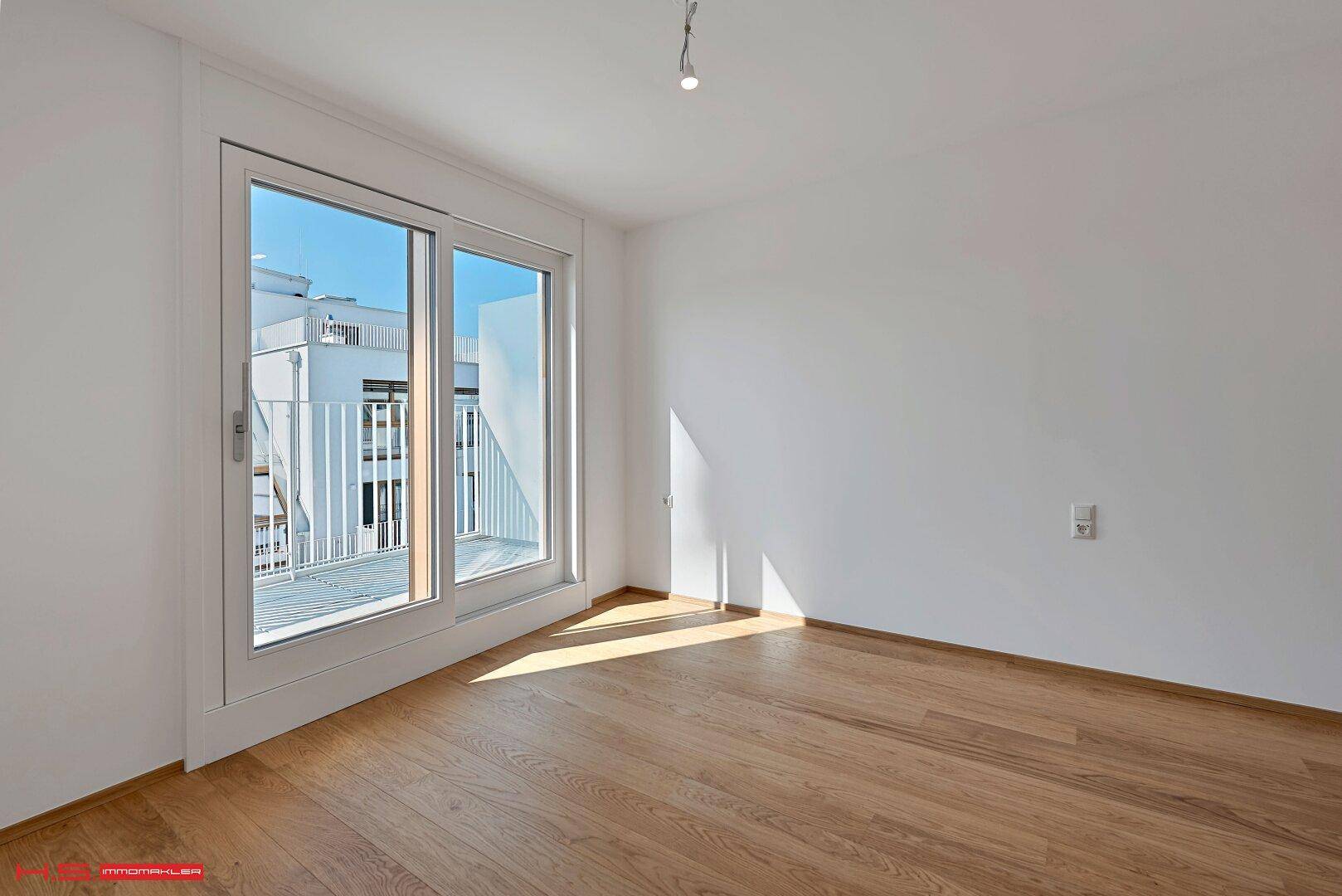 Helles Schlafzimmer mit Holzboden und Zugang zu einem kleinen Balkon, ideal für Morgenkaffee.
