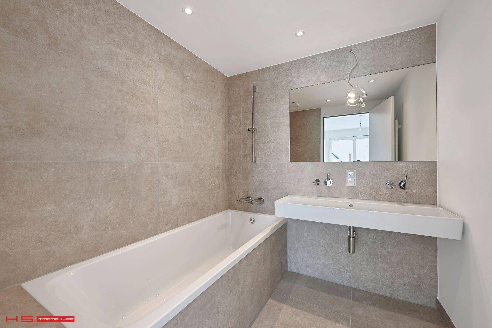 Modernes Badezimmer mit Badewanne, großem Spiegel und eleganten Fliesen an Wänden und Boden.