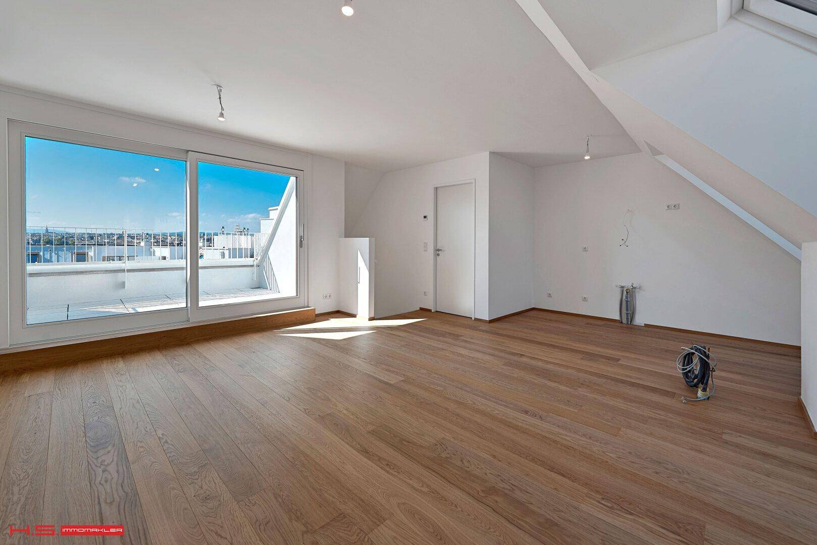 Großer, heller Raum mit Holzboden und Schiebetüren, die zu einer sonnigen Terrasse führen.