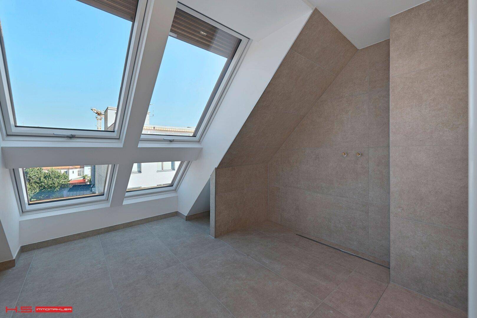 Modernes Duschbad im Dachgeschoss mit großen Dachfenstern und eleganten Fliesen an Wänden und Boden.